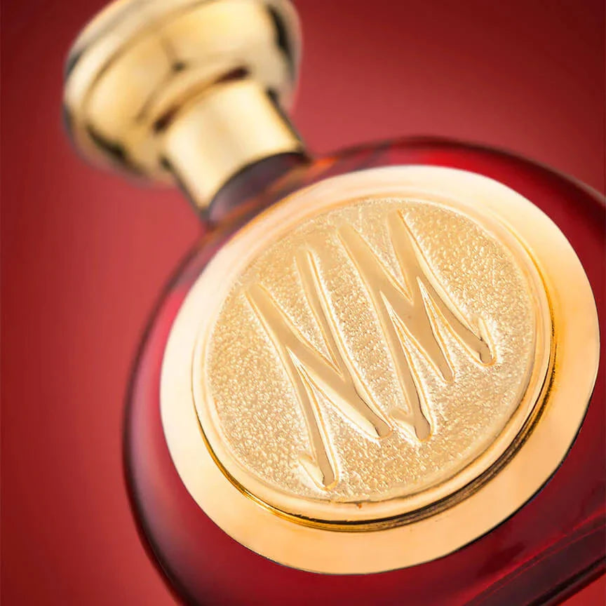 Close-up of a red and gold perfume bottle with a prominent logo on a red background